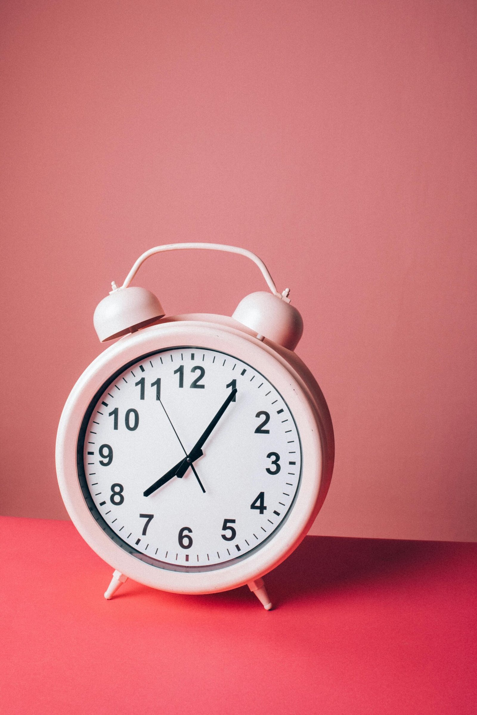A charming pink alarm clock standing on a pastel pink surface, embodying simplicity and elegance.